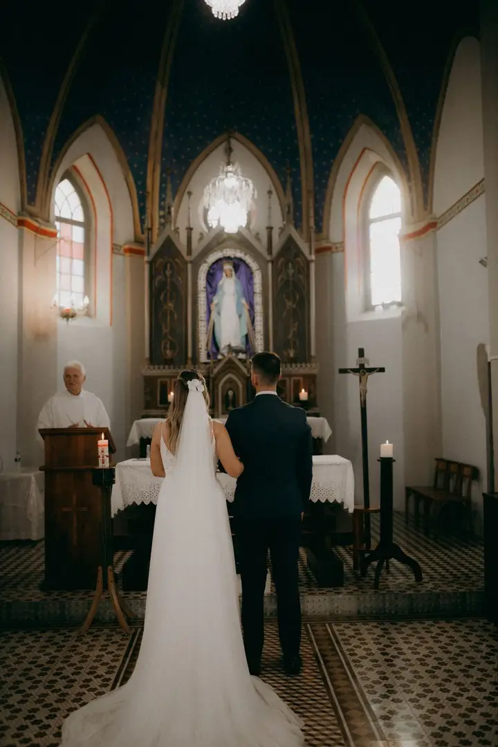 Bride and groom standing before a priest in a candlelit chapel